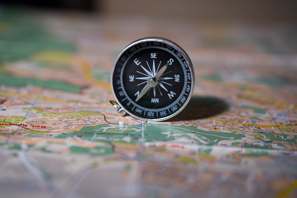 A baseplate orienteering compass resting on a topographic map with a mountain trail in the background