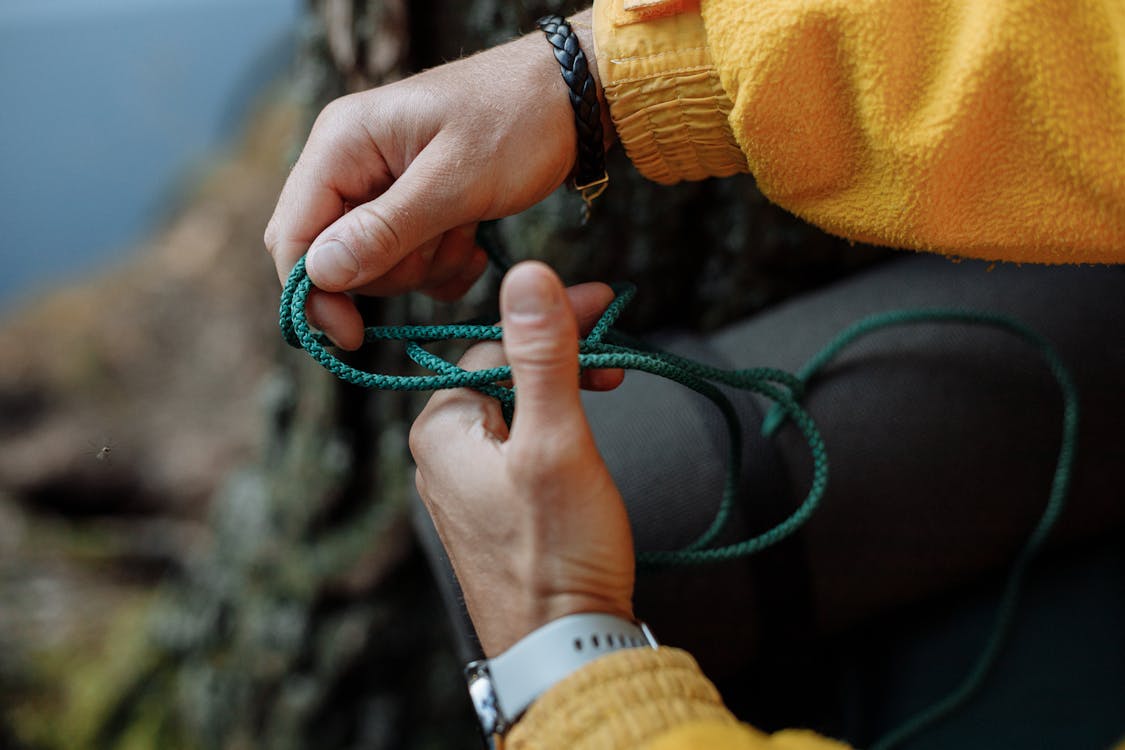 Hands tying a bowline knot with paracord on a tree branch in a forest