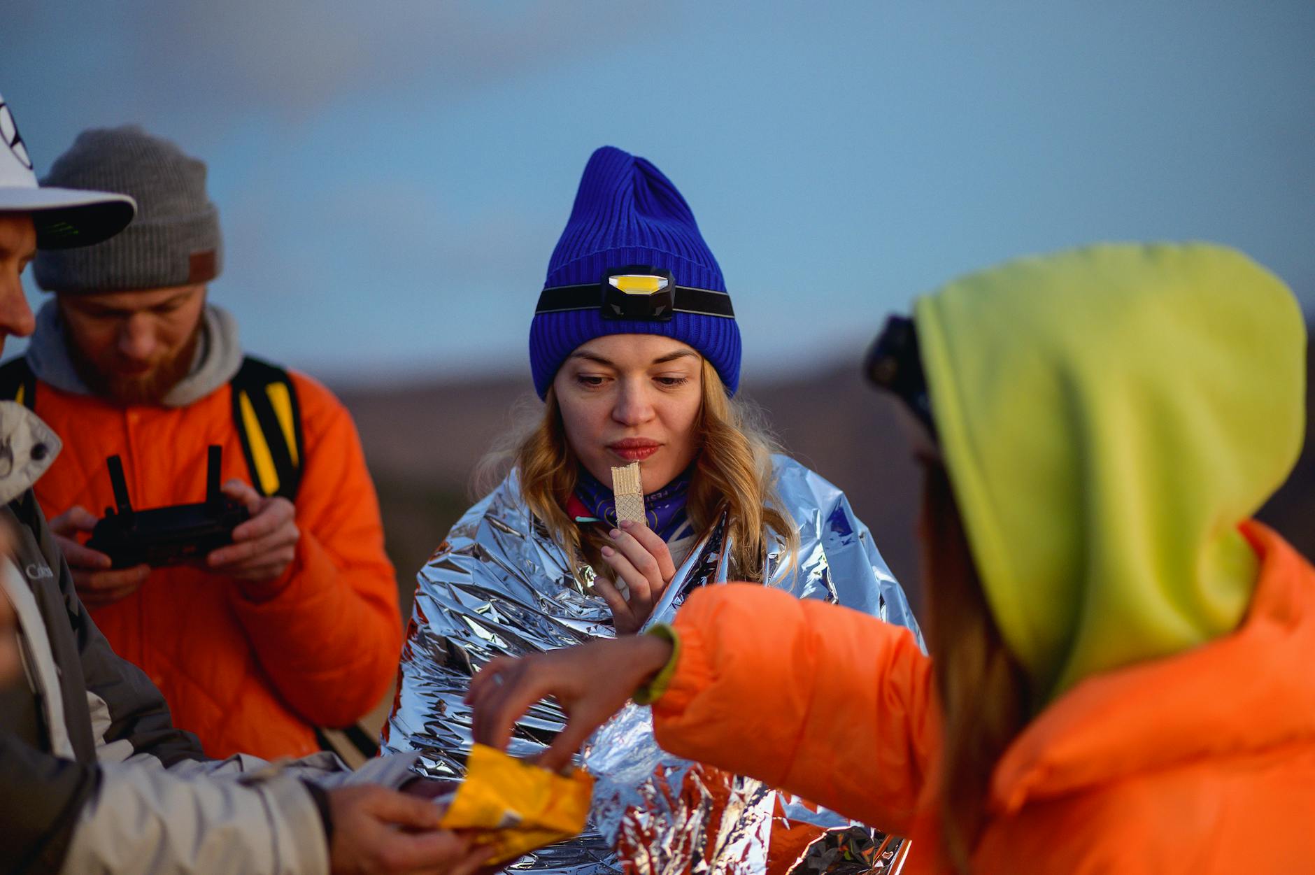 Person eating trail mix and energy bars beside a fire in a cold outdoor survival camp