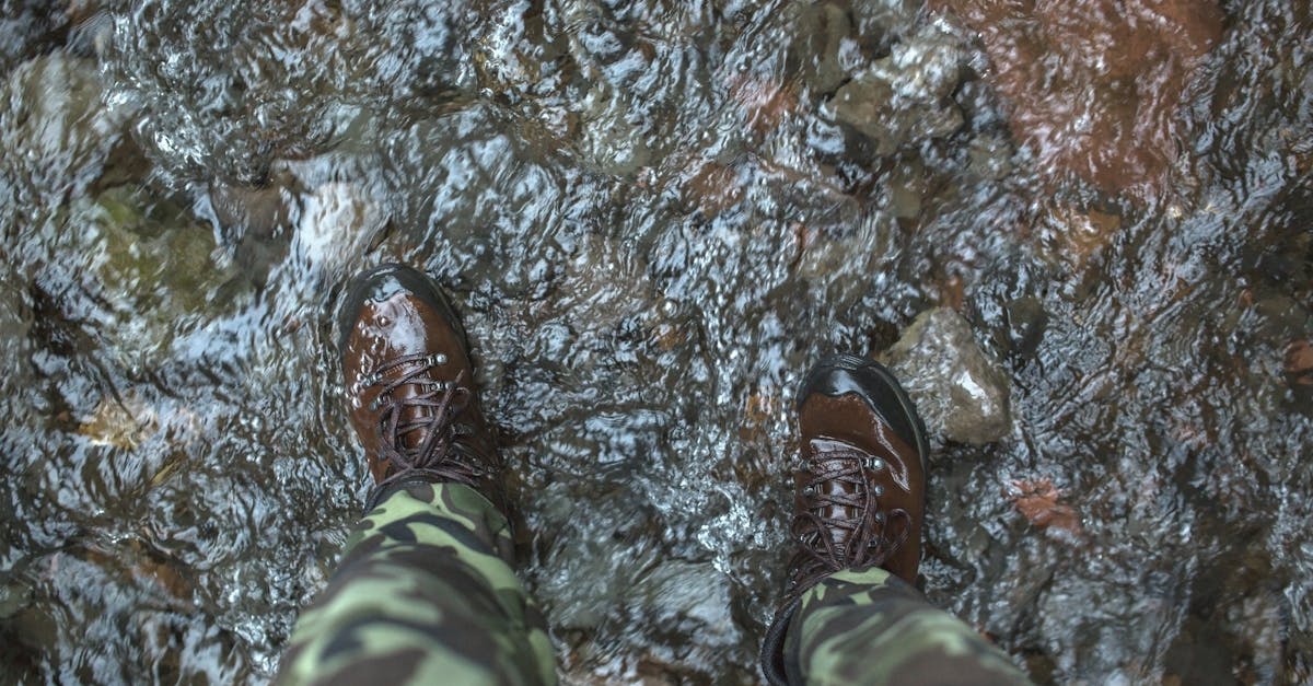 Person crossing a mountain river using trekking poles for stability