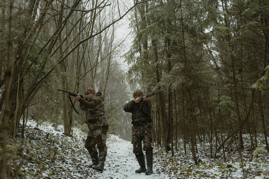 A hunter moving through dense woodland with a pack and rifle at dawn