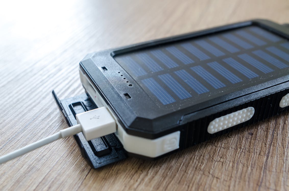 A portable solar panel charging a power bank on a rock in a sunny wilderness setting