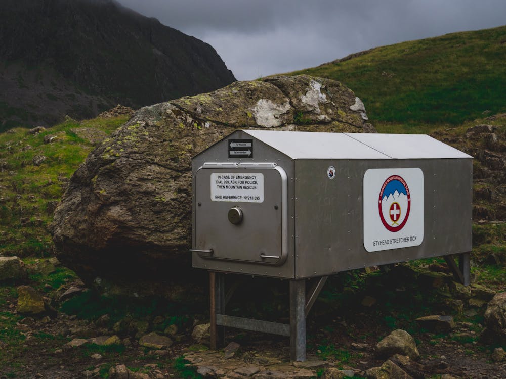 A first aid kit opened on a forest floor next to a hiking backpack